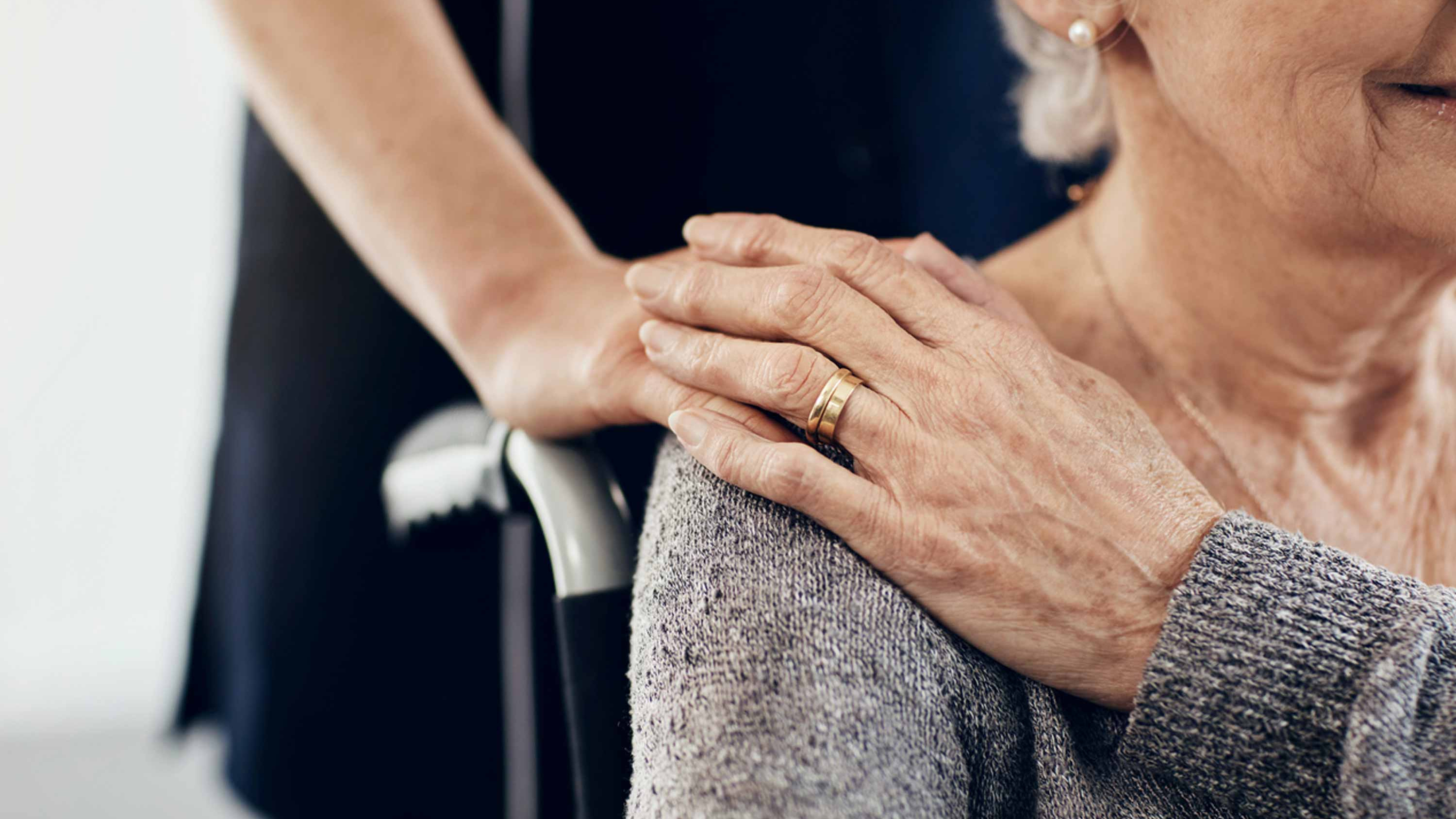 Woman in wheelchair pats caregiver's hand