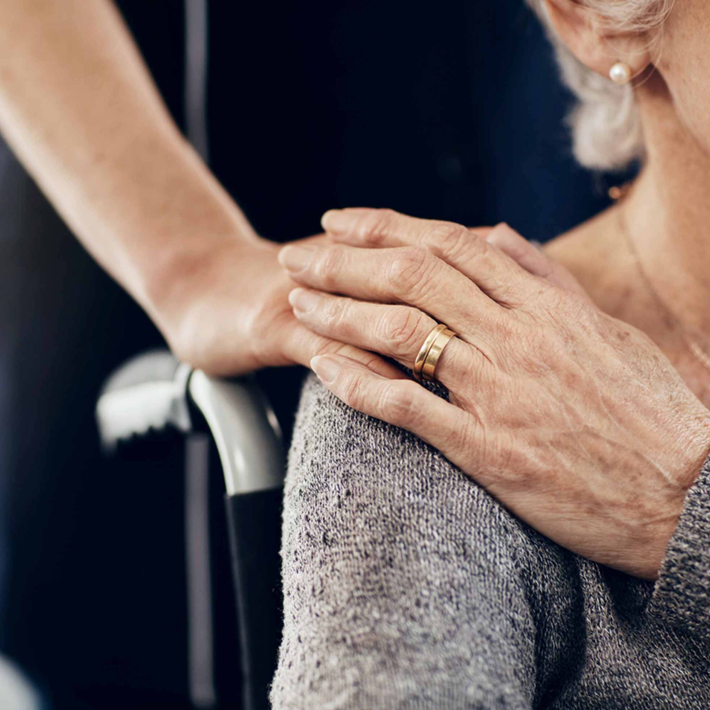 Woman in wheelchair pats caregiver's hand